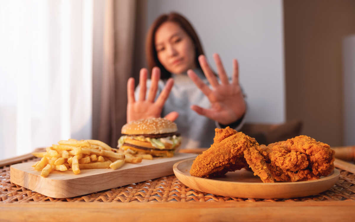 A woman making hand sign to refuse a hamburger, french fries and fried chicken on the table for dieting and healthy eating concept